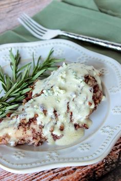 a white plate topped with meat covered in gravy and garnished with rosemary