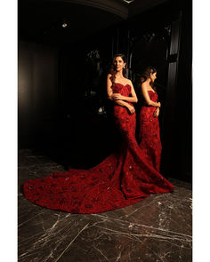 two women in red dresses standing next to each other on a marble floor with black walls