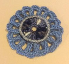 a crocheted blue and white flower on a yellow table top with a black center