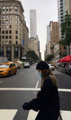 a woman wearing a face mask walking across a cross walk in the middle of a city