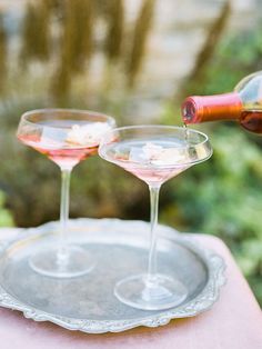 two wine glasses on a tray being filled with pink liquid by a bottle in the background