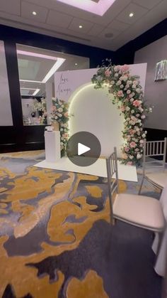 a white chair sitting in front of a flower covered stage with flowers on the wall