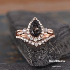 an engagement ring with a pear shaped black diamond surrounded by pearls on top of a rock