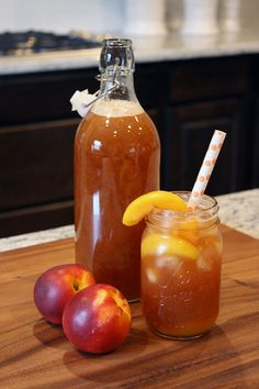 two jars filled with liquid sitting on top of a wooden table next to apples and oranges