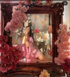 a woman sitting in front of a mirror with pink flowers around her and an ornate frame