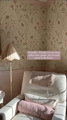 a white couch sitting under a lamp next to a wallpaper covered in pink flowers