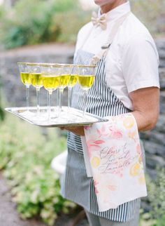 a man in an apron holding a tray with three glasses of wine and a note