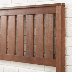 a close up of a wooden headboard against a white brick wall with wood slats