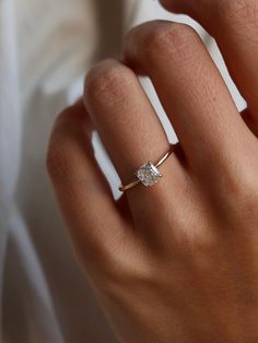 a woman's hand wearing a gold ring with a diamond in the middle and a white background