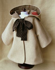 a doll is dressed in a coat with a bow on the collar and neckline