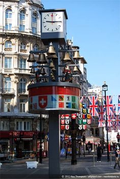 a clock tower in the middle of a street with flags hanging from it's sides