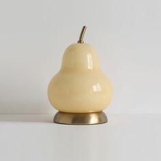 a yellow ceramic pear sitting on top of a white table next to a silver base