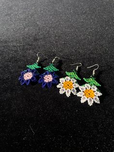 three earrings with flowers on them sitting on a black surface and one is made out of beads