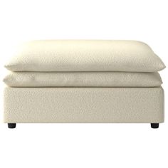 a white ottoman with two pillows on the top and one foot resting against it's back