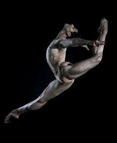 a male ballet dancer in the air with his legs spread out and one leg bent