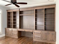 an empty room with wood floors and built in bookcases, ceiling fan and window