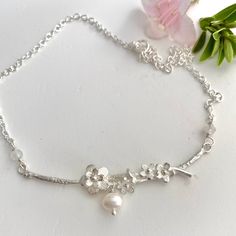 https://carolinebrookjewelry.etsy.com Compete your bridal look with grace when you choose our Chery Blossom, Silver, Pearl and Moonstone necklace. A delicate and carefully handcrafted piece, it embraces the undeniable beauty of nature. A curved and organically textured bar plays host to a cluster of detailed blooms, Moonstone beads and freshwater pearls. One would be forgiven for thinking it plucked off the woodland floor as if previously woven together by the fairies.  The necklace is designed to sit flush on the skin and compliments a multitude of dress styles, including those with jewel, straight or sweetheart necklines.  Choose the accessory that will accompany you down the aisle and become a much cherished family heirloom in no time. Made from 100% Sterling Silver dimensions: The Cher Wedding Necklace Simple, Nature Inspired Wedding Ring, Nature Wedding Ring, Oak Leaf Necklace, Cherry Blossom Necklace, Delicate Silver Necklace, Nature Inspired Wedding, Bridal Pearl Necklace, Pearl Jewelry Wedding