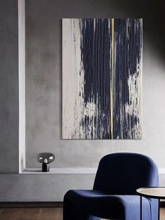 an abstract painting hangs on the wall above a blue chair and table in a living room