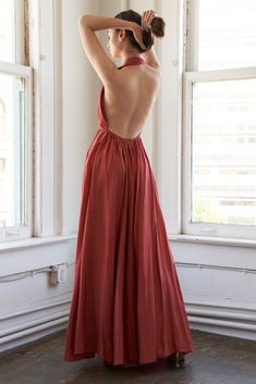 a woman in a long red dress standing by a window with her back to the camera