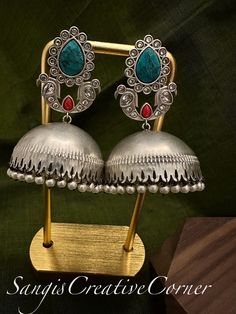 This brass-based textured silver tone finish jhumka style earrings has a very contemporary style with monalisa stone work with pearl embellishments. There are three variations to this piece based on the main monalisa stone: Yellow/Red, Turquoise/Coral, Mint/Red.  The combination of multi stone color with a silver tone brass-based metal finish will surely make you look royal and regal. It's the right balance you need to make a statement but not over the top.     Highlights of the piece: ** Dangle Handmade Fusion Style Ceremonial Earrings, Ceremonial Silver Bridal Earrings With Intricate Design, Ceremonial Bridal Earrings With Intricate Design In Silver, Handmade Silver Bridal Earrings For Festive Occasions, Silver Bridal Earrings With Intricate Design For Ceremonial Occasions, Handmade Fusion Style Dangle Jhumkas, Silver Meenakari Jhumkas For Rituals, Silver Tilla Earrings For Celebrations, Handmade Fusion Dangle Jhumkas