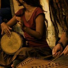 a woman sitting on the floor playing an instrument with other people around her looking at it