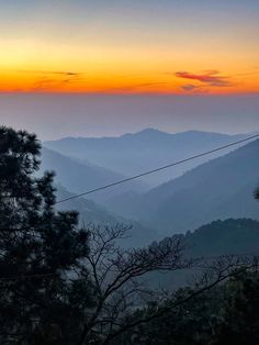 the sun is setting in the mountains with trees and power lines on each side,