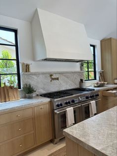 a stove top oven sitting inside of a kitchen next to a counter and sink with two windows