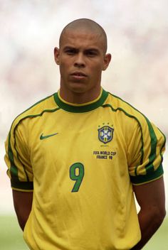 a soccer player is standing on the field with his hands in his pockets and looking at the camera