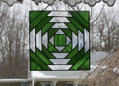 a stained glass window hanging in front of a house with snow on the ground and trees