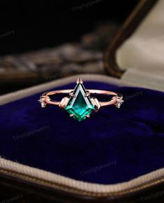 an emerald colored ring sitting on top of a velvet box