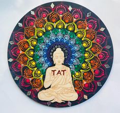 a buddha statue sitting in front of a colorful flower design on a circular wall hanging