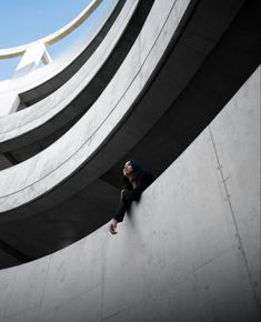 a woman sitting on the side of a building looking up at something in the sky