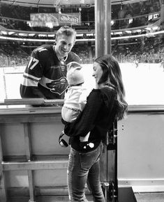 a woman holding a baby in her arms while standing next to an ice hockey player