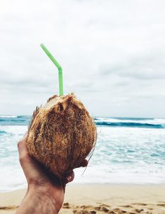 a person holding up a coconut drink on the beach