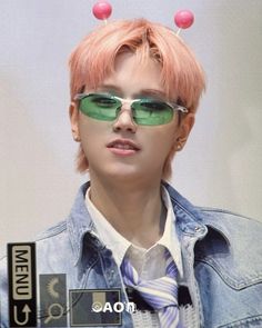 a man with pink hair wearing sunglasses and a blue jean jacket is looking at the camera