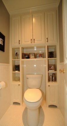 a white toilet sitting inside of a bathroom next to a walk in closet filled with cabinets