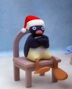 a penguin in a santa hat is sitting on a toy chair and looking at the camera