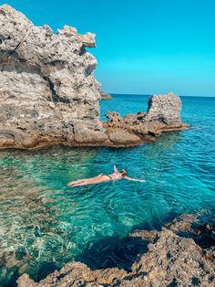 a person swimming in the ocean next to some rocks and blue water on a sunny day