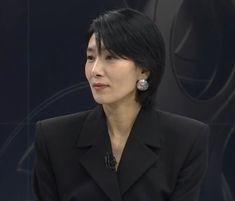 a woman with short black hair and earrings sitting in front of a microphone wearing a black suit