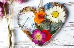 a heart shaped decoration with flowers hanging from it's side on a white wooden surface