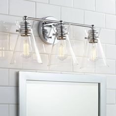 three light bathroom fixture with clear glass shades on the wall and white tile behind it