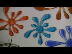 three different colored glass flowers on a white wall and one is blue, the other has orange