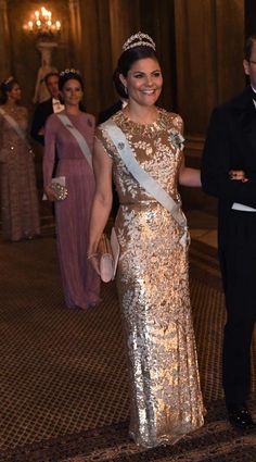 a woman in a gold dress is walking with a man