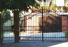 an iron gate is open on the side of a brick building with trees in front