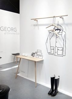 a white room with black and white drawings on the wall, clothes hangers and boots