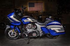 a blue and silver motorcycle parked in front of an american flag on the wall behind it