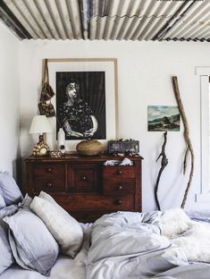 an unmade bed in a bedroom with white walls and wood accents on the ceiling