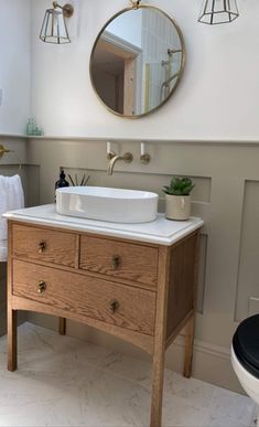 a white sink sitting under a bathroom mirror next to a wooden cabinet with drawers underneath it