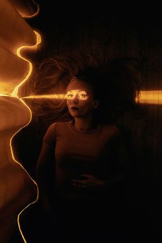 a woman standing in the dark with her hair blowing behind her and light shining on her face