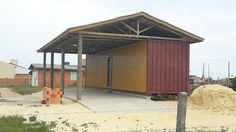 a building made out of shipping containers sitting on top of a dirt field next to a fence